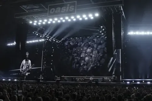حفل فرقة Oasis في استاد ويمبلي، حيث يظهر المغني وجمهور كبير، مع إضاءة ساطعة على المسرح.