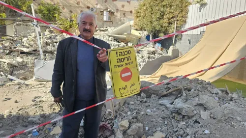 فخري أبو دياب يقف أمام أنقاض منزله المدمر في سلوان، مع لافتة تحذر من خطر الدخول، معبرًا عن شعور العجز بسبب التهجير.