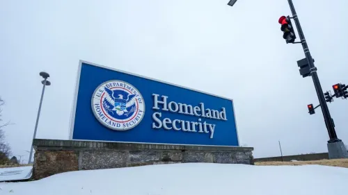 لافتة وزارة الأمن الداخلي الأمريكية في يوم ثلجي، تظهر شعار الوزارة مع إشارة مرور حمراء، تعكس القضايا المتعلقة بالهجرة والحماية المؤقتة.