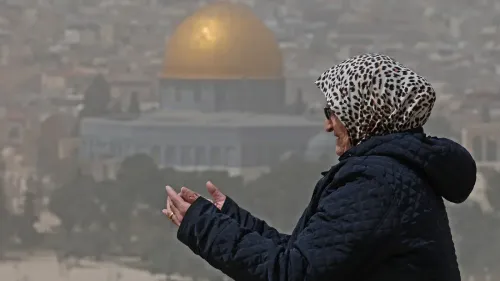 امرأة ترتدي حجابًا تقف وتدعو أمام قبة الصخرة في القدس، رمز المسجد الأقصى والتحديات التي تواجهه.