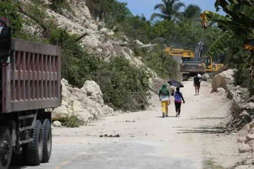 تظهر الصورة أشخاصاً يسيرون على طريق متضرر في الفلبين بعد الزلزال، بينما تظهر معدات ثقيلة في الخلفية تعمل على إزالة الأنقاض.