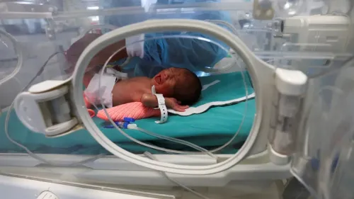 طفل حديث الولادة في حاضنة طبية، يعاني من حالة صحية حرجة، بينما يقوم أحد الأطباء بفحصه في مستشفى بغزة.