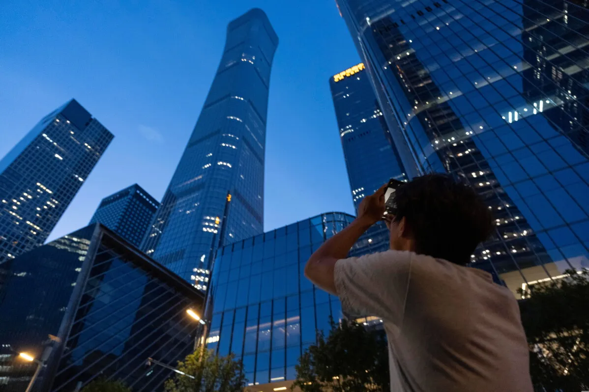 شخص يلتقط صورة لبرج CITIC الشهير في بكين، الذي يبلغ ارتفاعه 528 متراً، في وقت الغروب، مع وجود مباني حديثة حوله.