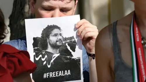 شخص يحمل لافتة تطالب بالإفراج عن الناشط المصري علاء عبد الفتاح، مع صورة له وخلفية تعبيرية تعكس التضامن والاحتجاج.