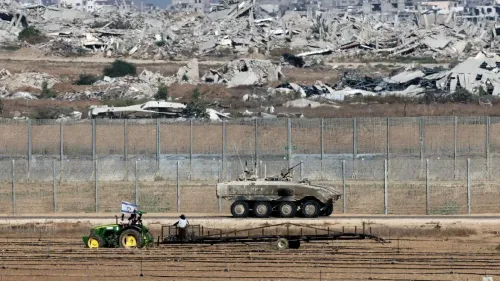 مشهد يظهر مزارع فلسطيني يقود جرارًا زراعيًا في حقل زراعي، بينما يمر مركبة عسكرية بالقرب من أنقاض المباني في غزة.