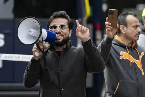 رجل يحمل ميكروفون ويعبر عن رأيه خلال احتجاج، بينما يقف رجل آخر خلفه يحمل هاتفه. الصورة مرتبطة بحادثة حرق القرآن في السويد.