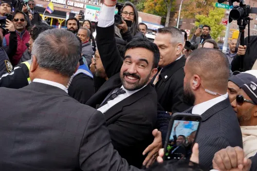 زهران ممداني، مرشح رئاسة بلدية نيويورك، يبتسم ويرفع يده وسط حشد من المؤيدين، مع وجود عناصر أمنية حوله.