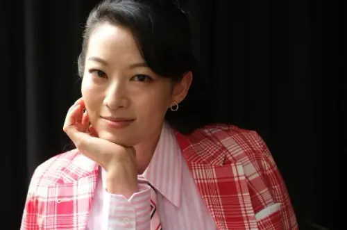 آردن تشو ترتدي بدلة مزخرفة باللونين الأحمر والأبيض، مبتسمة وتضع يدها على خدها، تعكس ثقتها بعد نجاح فيلم "KPop Demon Hunters".