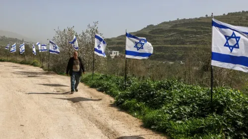 رجل يسير على طريق ترابي محاط بأعلام إسرائيلية، مما يعكس التوترات المستمرة في الضفة الغربية المحتلة.