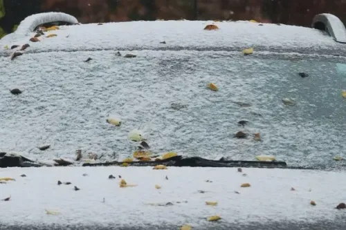 غطاء ثلجي كثيف يغطي زجاج سيارة مع أوراق شجر ملونة، مما يعكس الظروف الجوية الباردة المتوقعة في الولايات المتحدة.