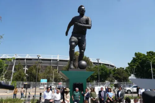 تمثال مكرس لأسطورة كرة القدم Pelé، يظهره وهو يركل الكرة، مع ملعب خلفه، خلال احتفال تكريمي.