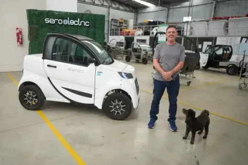 رجل يقف بجانب سيارة كهربائية صغيرة من طراز "سيرو إلكتريك" في ورشة عمل، مع كلب بجانبه، مما يعكس الابتكار في صناعة السيارات في الأرجنتين.