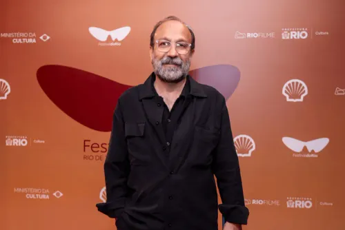 المخرج الإيراني أصغر فرهادي في مهرجان ريو السينمائي، مرتدياً نظارات وقميصاً أسود، مع خلفية تحمل شعار المهرجان وداعميه.