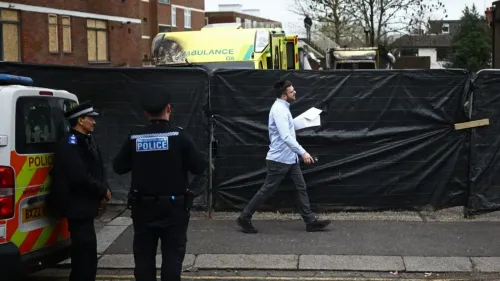 رجل يرتدي ملابس تقليدية يهودية يسير بجوار سيارات إسعاف متضررة ومحيط محاط بسياج أسود، بعد هجوم على سيارات إسعاف في لندن.