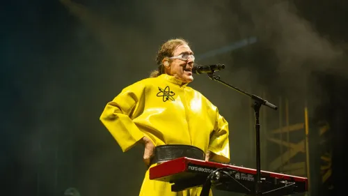 الفنان الكوميدي "Weird Al" Yankovic يرتدي زيًا أصفر مزينًا برمز ذرة أثناء أداء موسيقي على المسرح، احتفالًا بتكريمه بتسمية كويكب باسمه في حزام الكويكبات بين المريخ والمشتري.