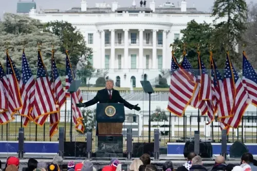 ترامب يتحدث أمام البيت الأبيض محاطًا بأعلام أمريكية، خلال تجمع قبل أحداث 6 يناير 2021، مما يبرز الجدل حول خطابه.