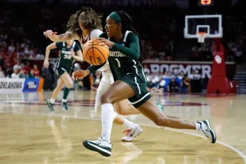 لاعبة كرة سلة من ولاية ميتشيغان تتقدم بالكرة، بينما تحاول لاعبة من أوكلاهوما الدفاع عنها في مباراة بطولة NCAA.