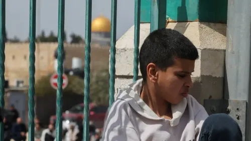 طفل يجلس على الأرض أمام بوابة المسجد الأقصى، مع قبة الصخرة في الخلفية، في ظل التوترات المستمرة حول الوصول إلى الموقع.