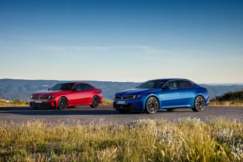 سيارتا BMW 3 Series 2027 باللونين الأحمر والأزرق متوقفتان على طريق ريفي، تمثلان مقارنة بين النسخة الكهربائية i3 ونسخة البنزين M350 ضمن فئة السيارات الفاخرة.