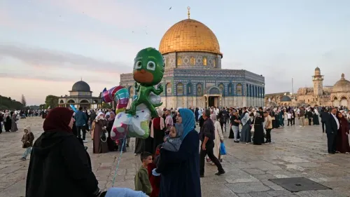 تجمع حشود من الزوار في ساحة المسجد الأقصى، مع وجود شخص يحمل بالوناً على شكل شخصية كرتونية، بينما يظهر القبة الذهبية للمسجد في الخلفية.