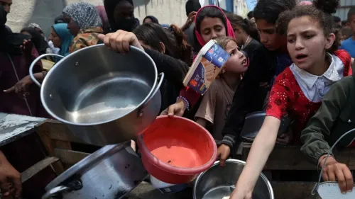 أطفال فلسطينيون في غزة يتجمعون حول نقطة توزيع الطعام، يحملون أواني فارغة في محاولة للحصول على المساعدات الغذائية وسط أزمة الحصار.