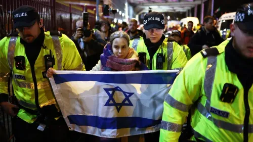 امرأة تحمل علم إسرائيل بينما يرافقها عناصر من الشرطة خلال احتجاج ضد حظر مشجعي مكابي تل أبيب في برمنغهام.