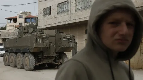 طفل يرتدي سترة رمادية يقف في الشارع بالقرب من مركبة عسكرية إسرائيلية، مما يعكس التوترات الحالية في المنطقة.
