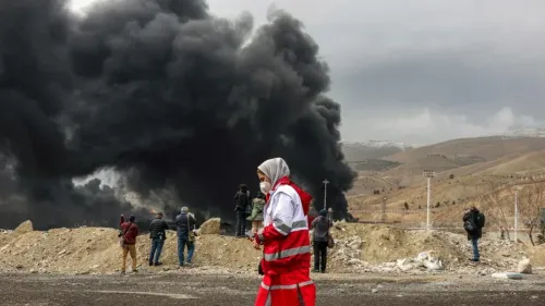 سحابة من الدخان الأسود تتصاعد في السماء بينما يتواجد أفراد من الطواقم الطبية والمراسلين في موقع الهجوم الإيراني، مع مشاهد للدمار في الخلفية.