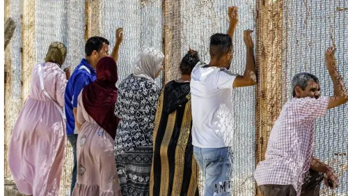 مجموعة من الأشخاص ينظرون عبر سياج حدودي بين المغرب ومدينة سبتة الإسبانية في سياق أزمة الهجرة والوفيات الجماعية.
