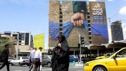 لوحة إعلانات ضخمة في طهران تظهر يدًا ممسكةً بعلم إيران، مع خلفية زرقاء وأسلحة، بينما يمر المارة والسيارات في الشارع.