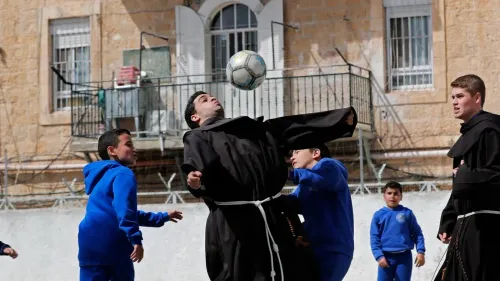 طلاب ومعلمون في مدرسة مسيحية في القدس يلعبون كرة القدم في ساحة المدرسة، تعبيرًا عن روح التعاون والمرح وسط التحديات التعليمية.