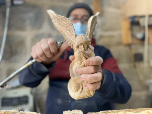 نحات فلسطيني يحمل تمثالًا خشبيًا ملائكيًا مزخرفًا، يظهر تفاصيل دقيقة في ورشة عمل في بيت لحم، رمزًا للتقاليد المسيحية.