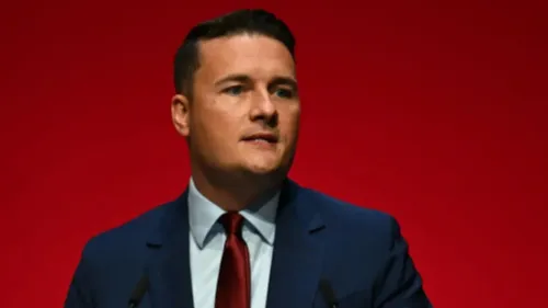 وزير الصحة ويس ستريتينغ يتحدث في مؤتمر، مع خلفية حمراء، وسط جدل حول دعم الحكومة البريطانية لإسرائيل وجرائم الحرب في غزة.