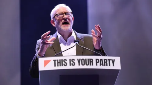 جيريمي كوربين يتحدث في مؤتمر، معبرًا عن انتقاده لحكومة حزب العمال بشأن عقد مع شركة بالانتير، مع خلفية تحمل شعار "هذه هي حزبك".