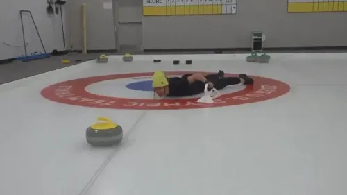 لاعب كيرلنج يتدرب على الجليد في مركز الكيرلنج، محاطًا بأحجار الكيرلنج، ويظهر التركيز على مهاراته قبل انطلاق المنافسات الأولمبية.