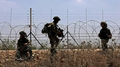 جنود إسرائيليون يتواجدون بالقرب من سياج حدودي، مع وجود أسلاك شائكة وأرض جافة، مما يعكس التوترات في المنطقة.