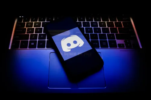 شعار تطبيق Discord على شاشة هاتف ذكي موضوع على لوحة مفاتيح كمبيوتر محمول مع إضاءة خافتة، يعكس موضوع التحقق من العمر وحماية المستخدمين على منصة الدردشة.