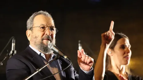 إيهود باراك يتحدث في حدث عام، مع وجود امرأة تشير بلغة الإشارة بجانبه، وسط أضواء خافتة.