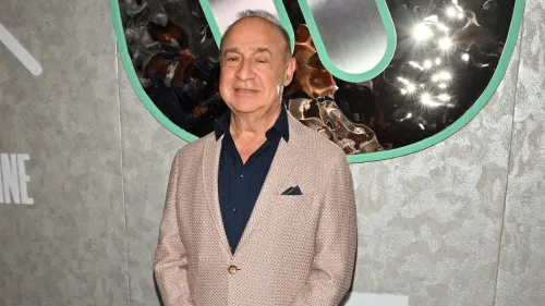 صورة لرجل مسن يرتدي سترة رمادية وقميص أسود، يقف أمام جدار مزخرف، يعكس علاقته مع جيفري إبشتاين وأحداث اجتماعية بارزة.