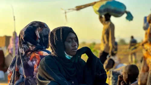 امرأة سودانية ترتدي الحجاب تجلس بحزن وسط نزوح مدنيين في دارفور، تعبيراً عن معاناة ضحايا الحرب والجرائم ضد الإنسانية.