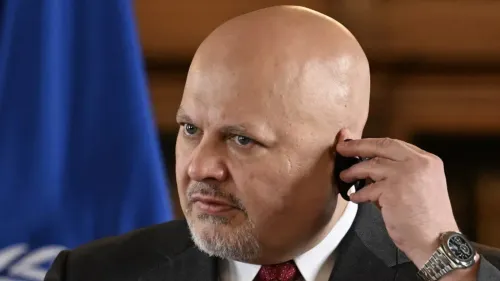 موظف في المحكمة الجنائية الدولية يتحدث عبر الهاتف، مع علم المحكمة في الخلفية، في سياق دعم عودة المدعي العام كريم خان.