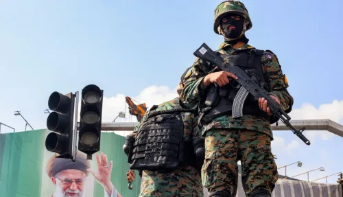 عناصر من القوات الأمنية الإيرانية يرتدون زيًا عسكريًا ويحملون أسلحة، يقفون بالقرب من إشارات المرور في مدينة إيرانية، مع صورة للمرشد الأعلى السابق خلفهم.