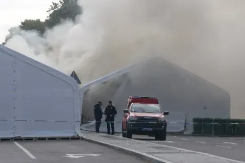 تصاعد الدخان من خيام في بلغراد بعد اندلاع حريق، بينما يتواجد ضباط الشرطة في الموقع مع سيارة إسعاف، في سياق أحداث سياسية متوترة.