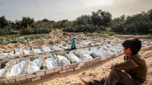 مقبرة جماعية في غزة تحتوي على جثث مغطاة بأقمشة بيضاء، بينما يتجول طفلان بين القبور، مما يعكس آثار العدوان الإسرائيلي المستمر.
