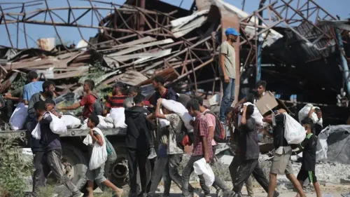 أطفال وراشدون يحملون مساعدات إنسانية في غزة، مع خلفية لمباني مدمرة، في سياق الأزمة الإنسانية المتفاقمة جراء الحرب.