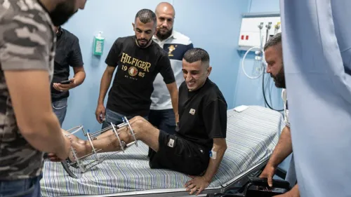شاب فلسطيني مصاب بجروح في ساقه داخل مستشفى في غزة، محاط بأشخاص يقدمون له الدعم والرعاية الطبية.