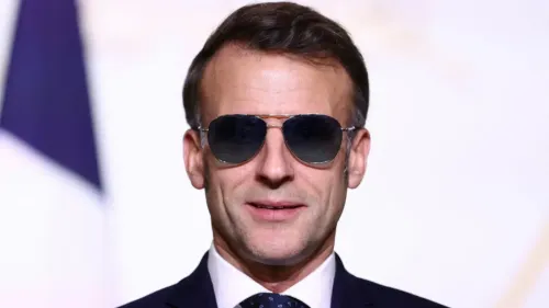 ماكرون يرتدي نظارات شمسية، مع تعبير واثق، في سياق مناقشات حول تصنيف الحرس الثوري الإيراني كمنظمة إرهابية.