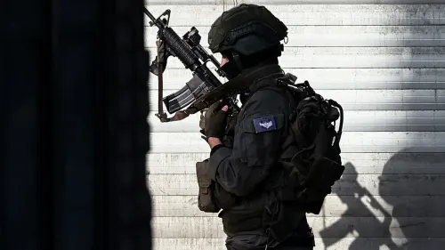 جندي إسرائيلي مسلح يقف بجانب جدار أثناء مداهمة في الضفة الغربية، مما يعكس التوترات المستمرة وتأثيرها على الفلسطينيين.