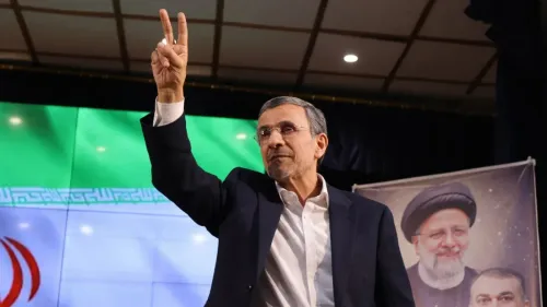 الرئيس الإيراني السابق محمود أحمدي نجاد يرفع إصبعيه في إشارة النصر، خلفه علم إيران، تعبيراً عن عودته المحتملة إلى الساحة السياسية.