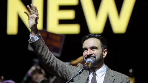 ممداني، السياسي الشاب، يلوح بيده خلال خطاب في نيويورك، مع خلفية تحمل كلمة "NEW"، معبرًا عن رؤيته للمساواة والعدالة.